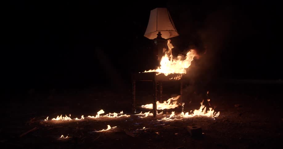 Flames flicker and burn around and on a table with a lamp on it