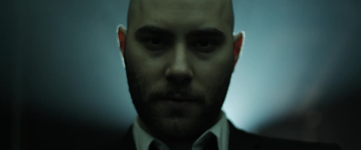 A man in a suit and tie stands in front of a bright color changing light