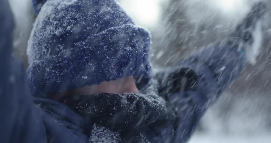 A boy is bundled up in a coat and hat as he throws snow in the air