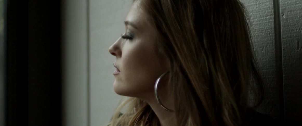 A woman running a hand through her brown hair while leaning against a wall