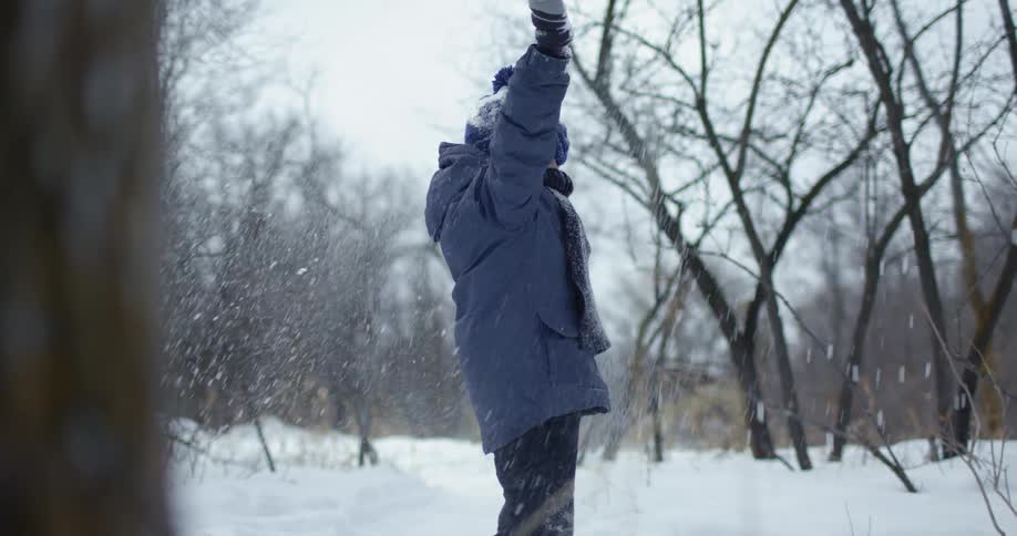 Young boy wearing a parka plays with snow balls on a forest at winter