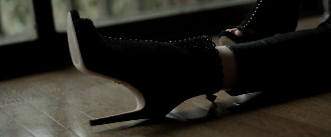 A woman wears high heeled sandals as she sits outside on the floor of her balcony