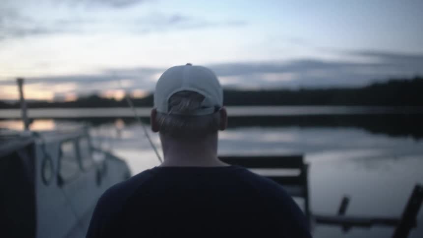 A man carrying a fishing pole walks on a pier at dusk