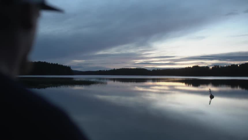 A man looks across a lake at sunrise