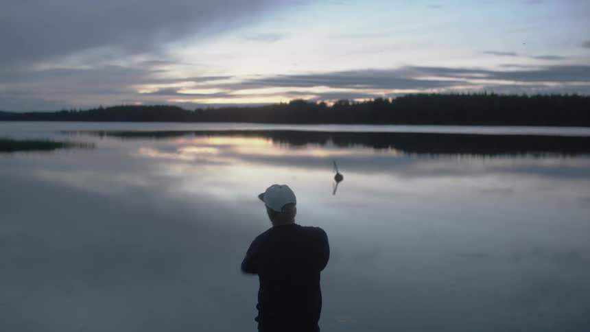 A man casts a fishing line into a lake at dawn