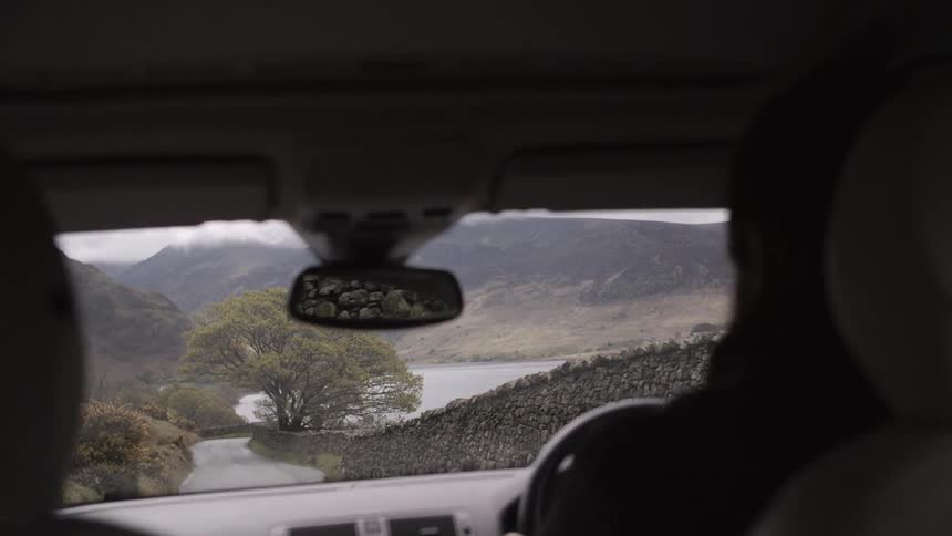 A vehicle is moving down a road lined with a stone wall