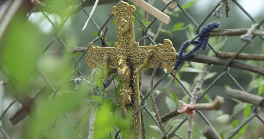 A small gold cross is tied with pipe cleaners to a chain link fence