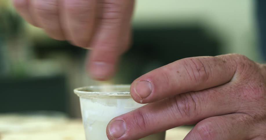 Hands hold a small container as a stick is used to stir a white paste