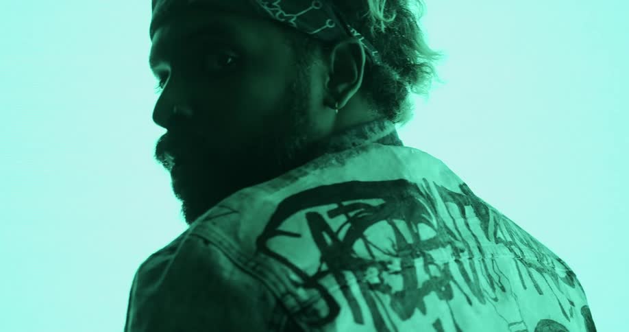 A man with a headband and a jacket in a room next to a big screen