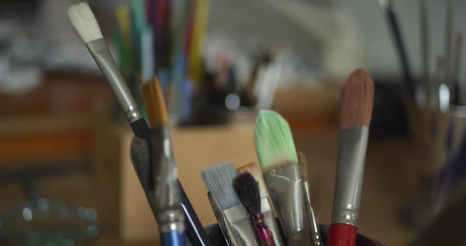 A view of paintbrushes and pencils that are in cups on a table