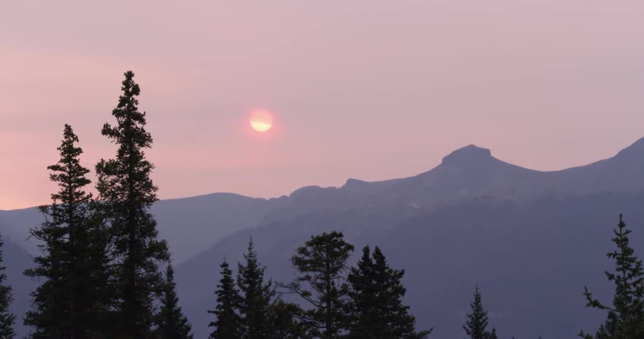 The sky is pink as the sun sets over a mountain range and forest