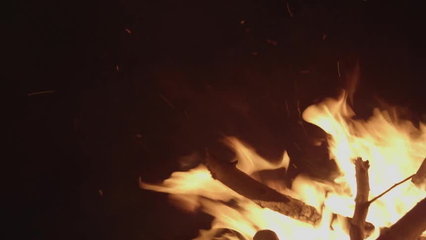 A fire made of a pile of sticks grows taller and sends sparks flying into the air