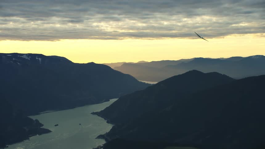 Aerial shot of a glider plane soaring above the Columbia River Gorge in Oregon and Washington as it makes a massive turn to the right side of the frame at sunset