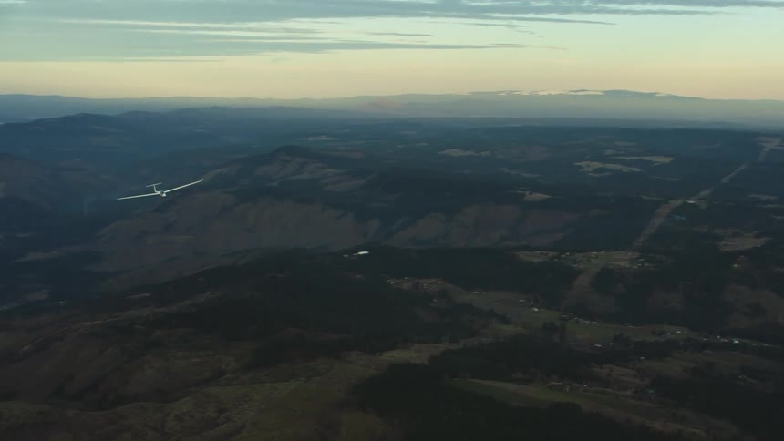 A glider airplane is towed high above the earth before releasing its tow line and the gliding free while the tow airplane dives towards the ground revealing a beautiful snow covered Mount Adams at sunset