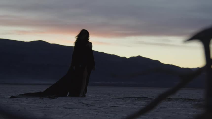 A model in a flowy robe walks through the desert barefoot at dusk