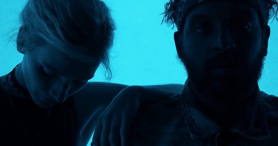 A woman with her hand resting on a mans shoulder lowers her head down