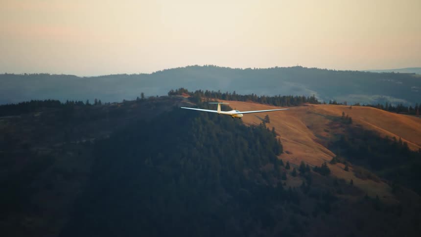 Tight shot of a white glider airplane soaring high above golden hills at sunset in this dramatic air to air aerial shot