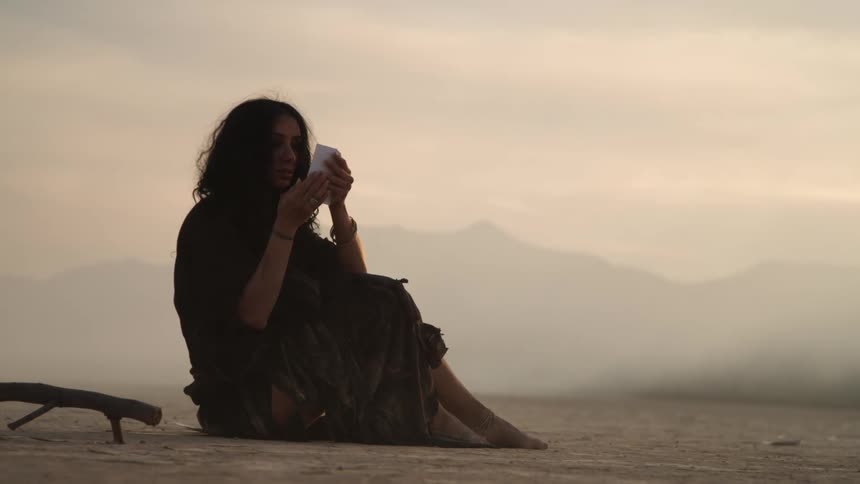 A woman sitting on a dry lake bed on her phone