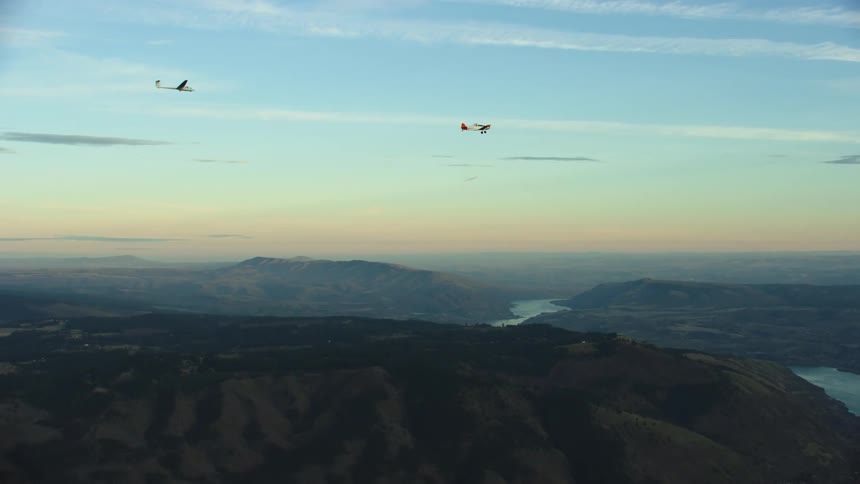 A small glider is being towed by a white and red single engine airplane high above the Columbia River gorge in this beautiful sunset aerial shot