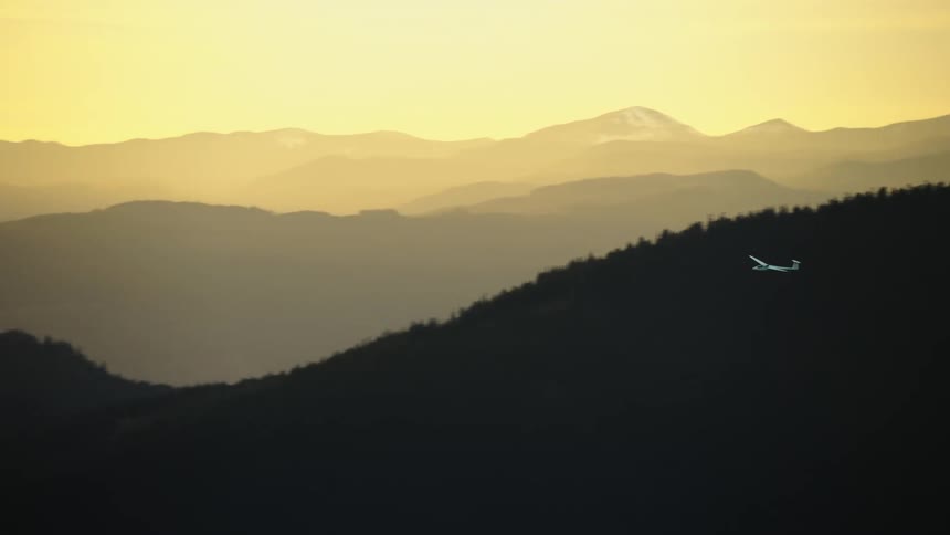 A white fiberglass glider aircraft soars high above ridges and a beautiful Columbia River Gorge at sunset in this air to air aerial highlighting the magic of flight with no engine