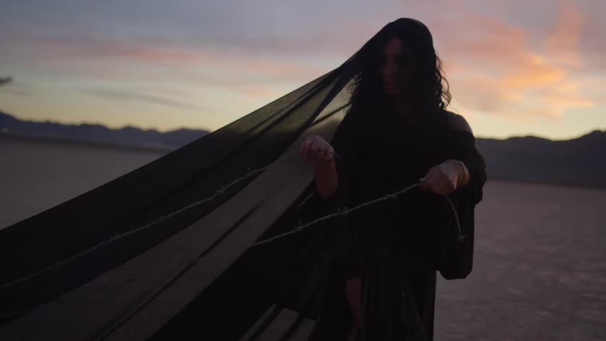 A woman dressed in black veil pulls branches through the desert using rope at sunset