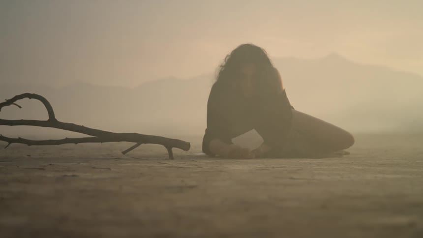 Woman lies on arid ground on dusty hazy day grasping paper