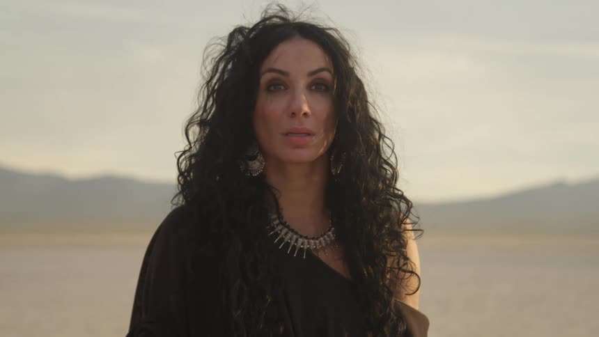 A woman poses in the desert in a flowing gown and necklace