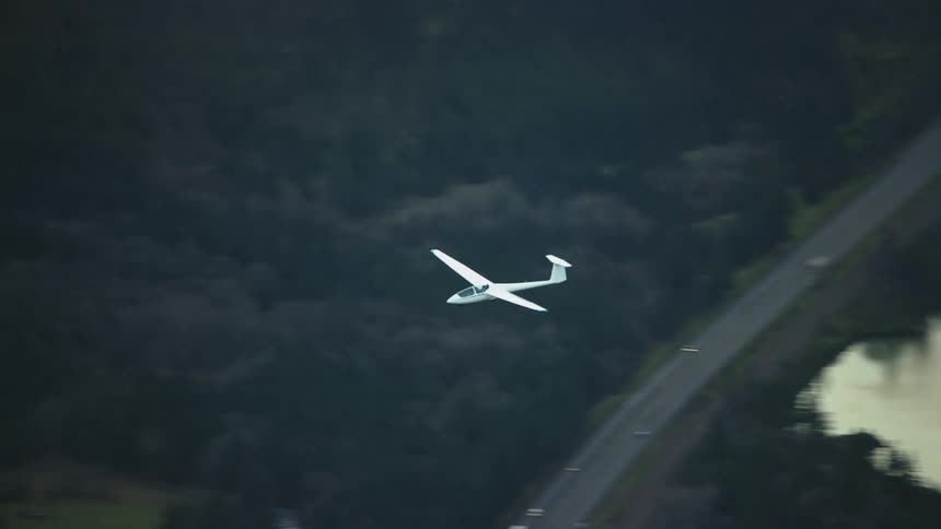 Tight shot of a white fiberglass airplane soaring high above the Columbia River Gorge in Washington and Oregon with contrasting water and tree terrain below