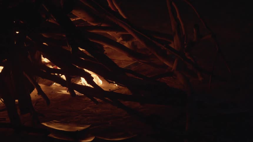A fire starts from below a pile of a sticks formed into hill in the desert