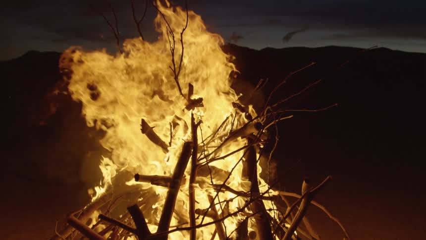 A bonfire made with tall sticks on a triangle formation burns in a desert at night