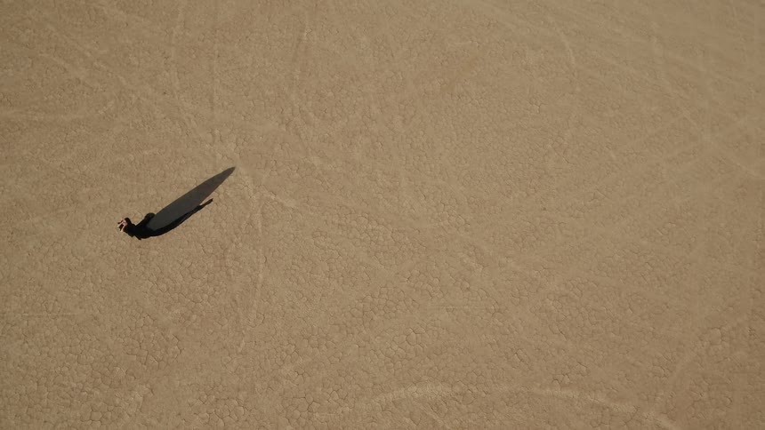 A woman in a long black dress walks through a vast dry desert
