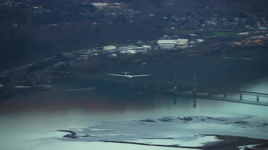 Blue hour post sunset air to air aerial shot of a white glider airplane with no engine soaring above the Columbia River and the Hood River bridge in this air to air aerial