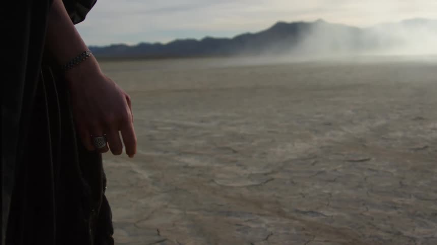 A person in dark robes stands in the desert