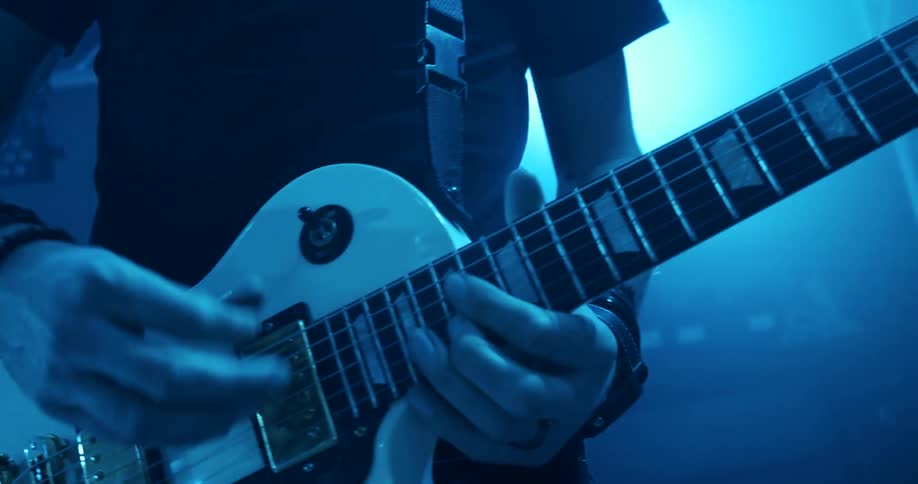 Musician playing electric guitar on stage under blue lights