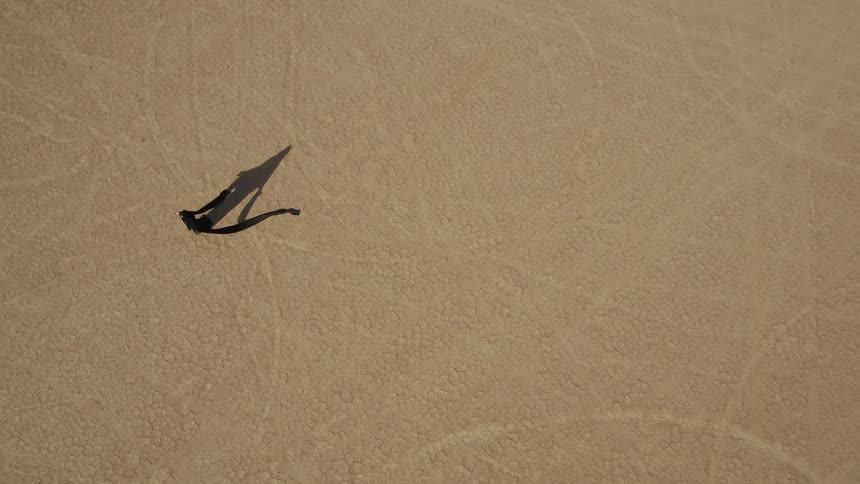 Person wearing black with long train casts shadow on sands