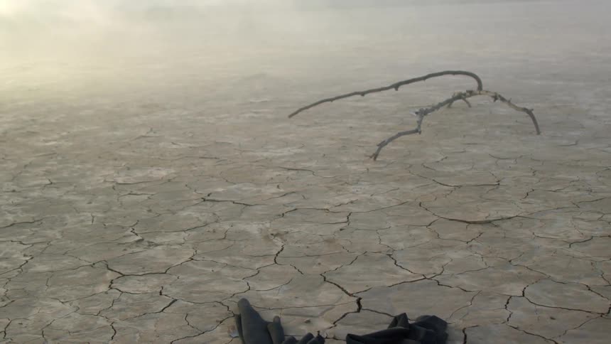 Dark fabric drags across arid ground away from fog and branch