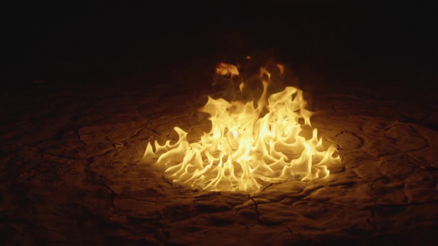 Flames covering an area of ground are burning in the darkness