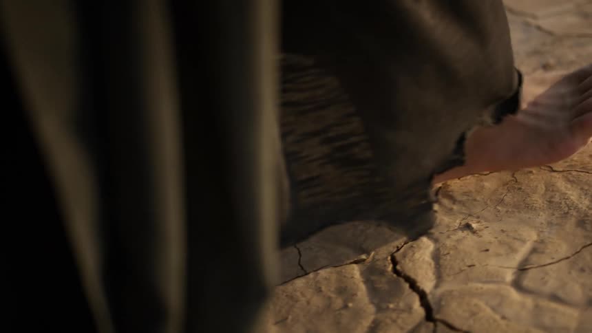 A person in long dark robes walks in the desert