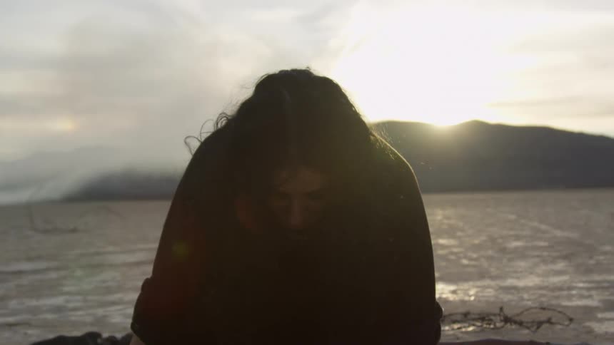 A woman crawling on her hands and knees in a desert puts her head towards the ground