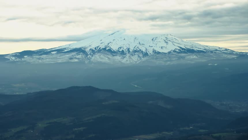 A gilder airplane soars high above the Cascade Mountains in the Pacific Northwest in this sunset air to air aerial in Hood River Oregon