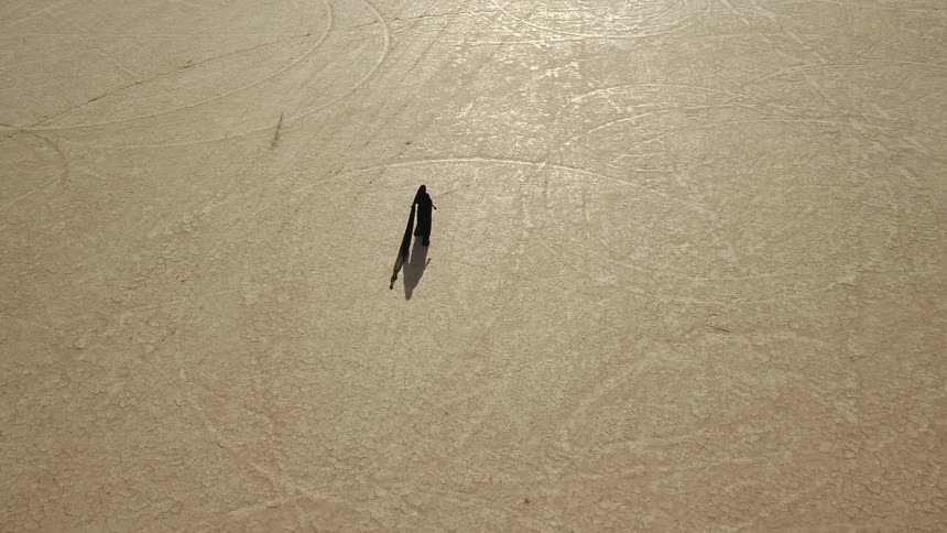 A woman with a long black veil walking alone in a sandy desert