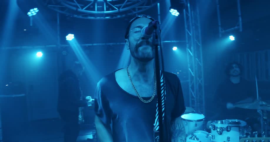 A man sings and plays his guitar on stage in front of his band members