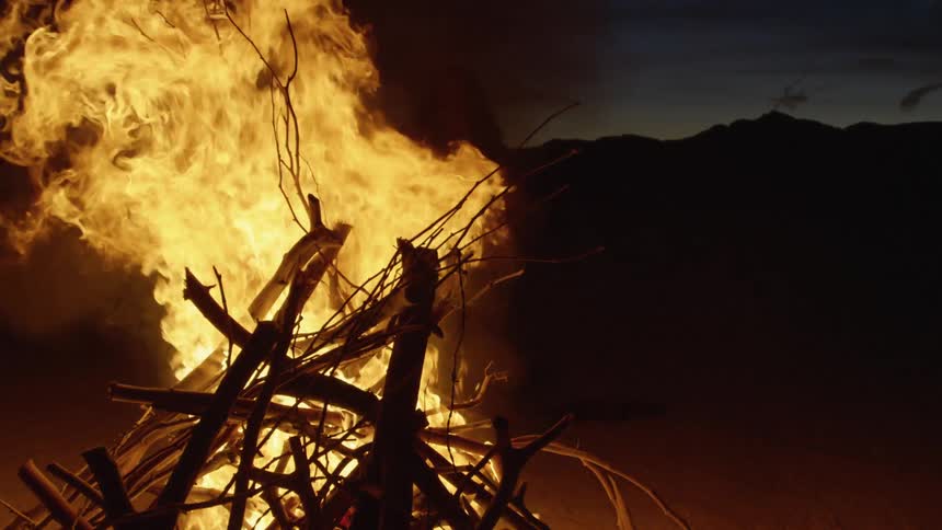 A woman stands and watches a fire in the desert as flames come near her