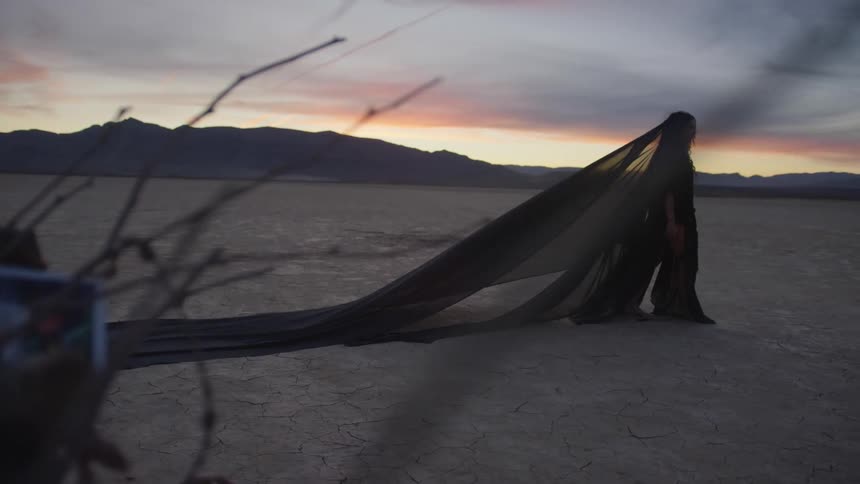 A woman in long black robes walks in the desert
