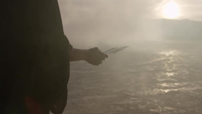 Person carries sheet through foggy area toward cloud obscured sun peaking over mountain