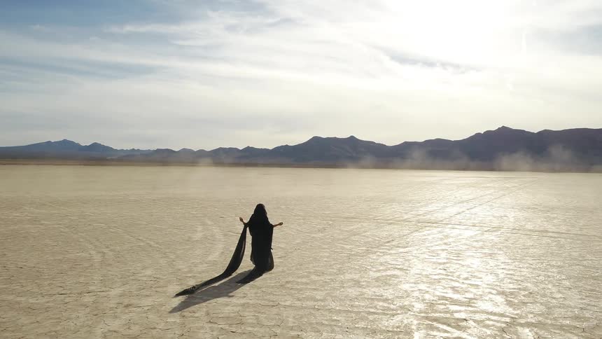 A woman in black with dragging veils walks through the desert