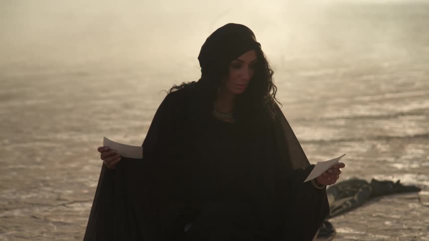 A woman is standing outdoors by the ocean at dusk