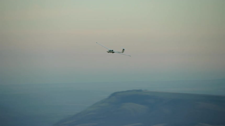A white glider airplane soars above many ridges in a blue hour spectacular late evening air to air aerial shot