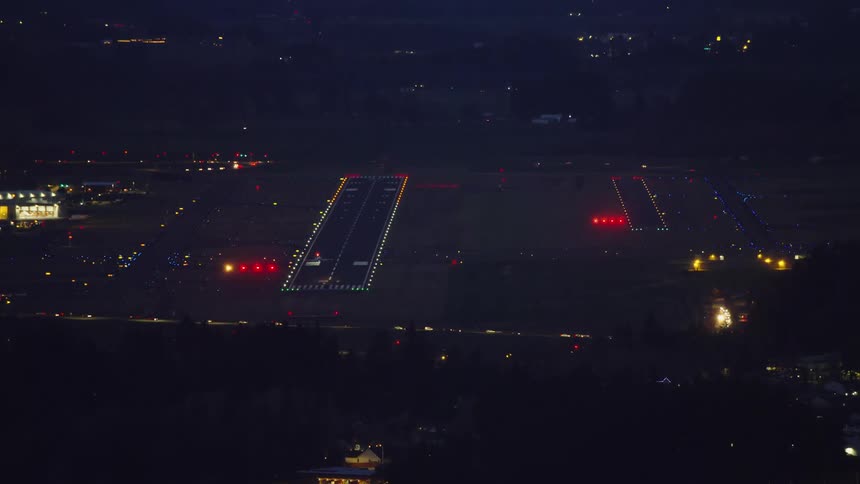 Wide shot of a private jet on final approach to land at a large airport and eventually touches down at the end of the shot in this blue hour air to air aerial shot