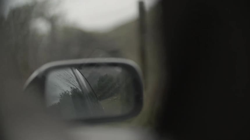 The rearview mirror of a car as it is traveling down a road